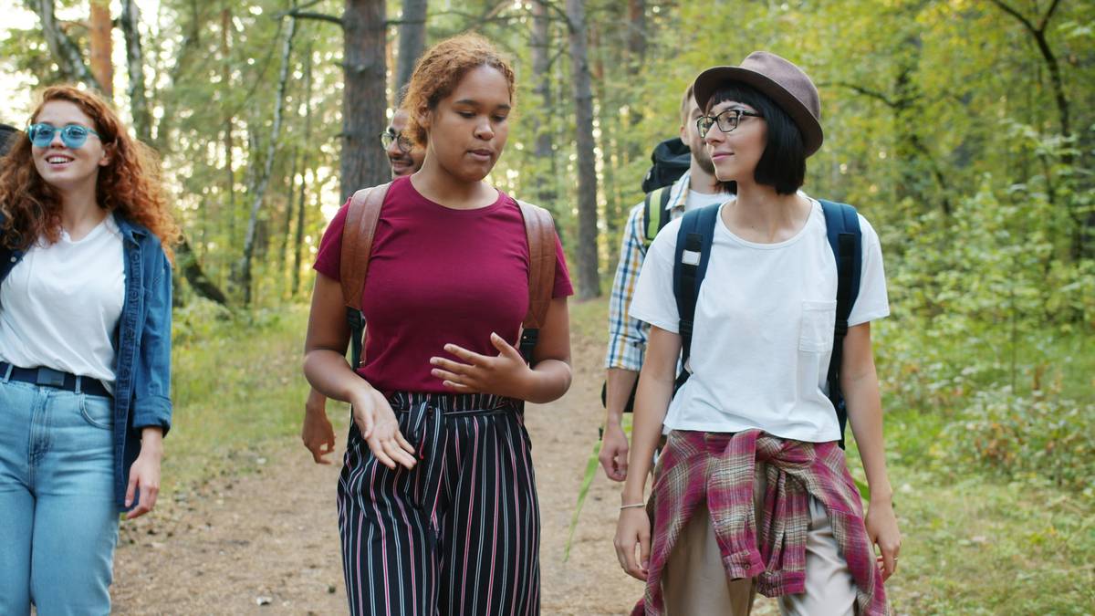 hiking tips for beginners: woman adjusting backpack on sunny forest trail with map in hand